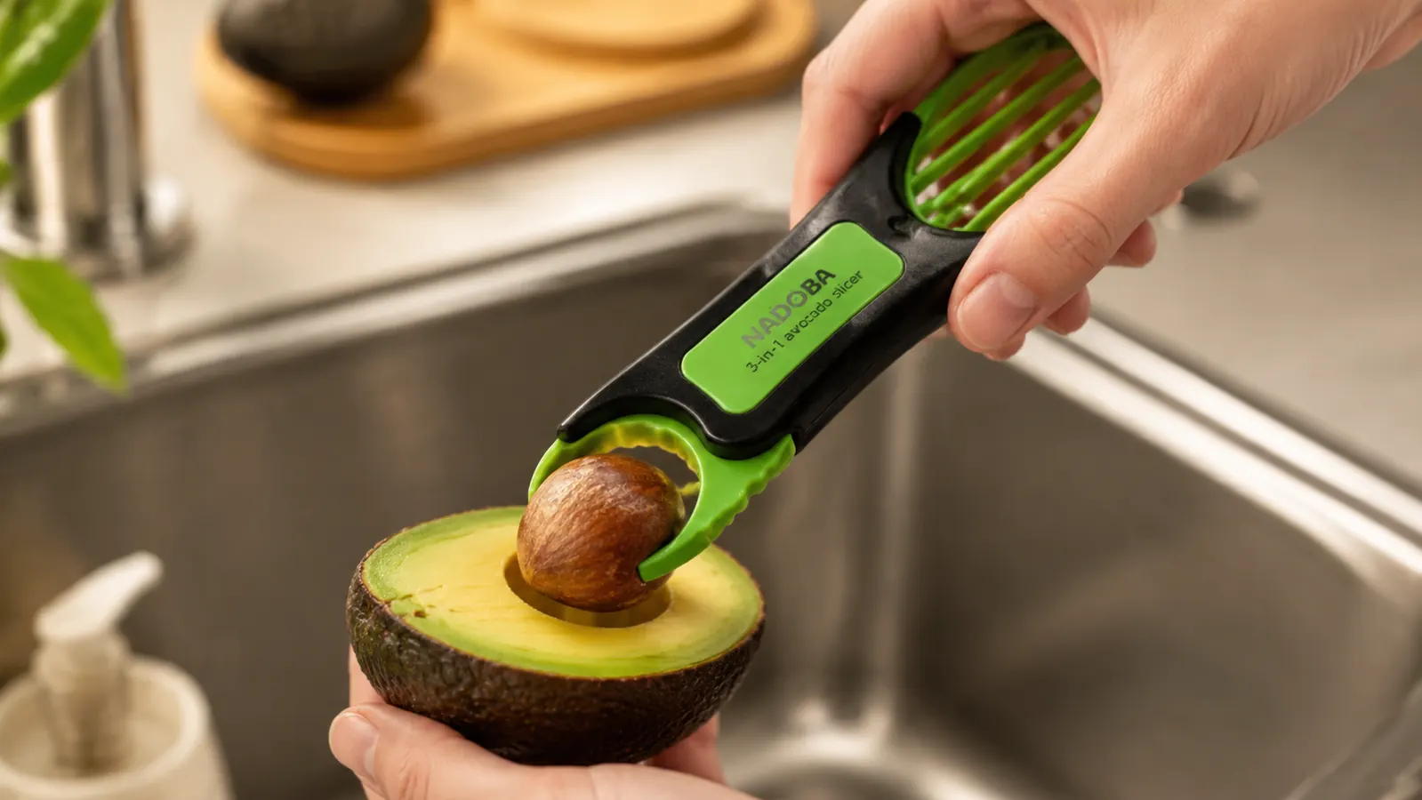 Hand using the avocado tool to pop the pit out of a halved avocado over a kitchen counter