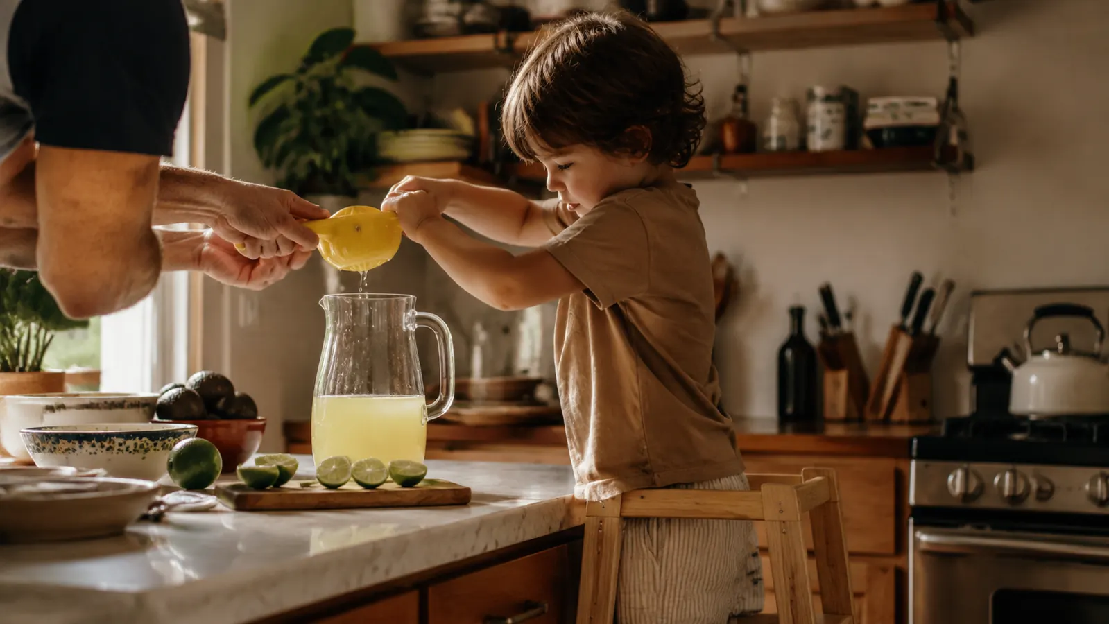 A child standing on a step stool helping squeeze a lime into a pitcher of iced tea at the kitchen counter