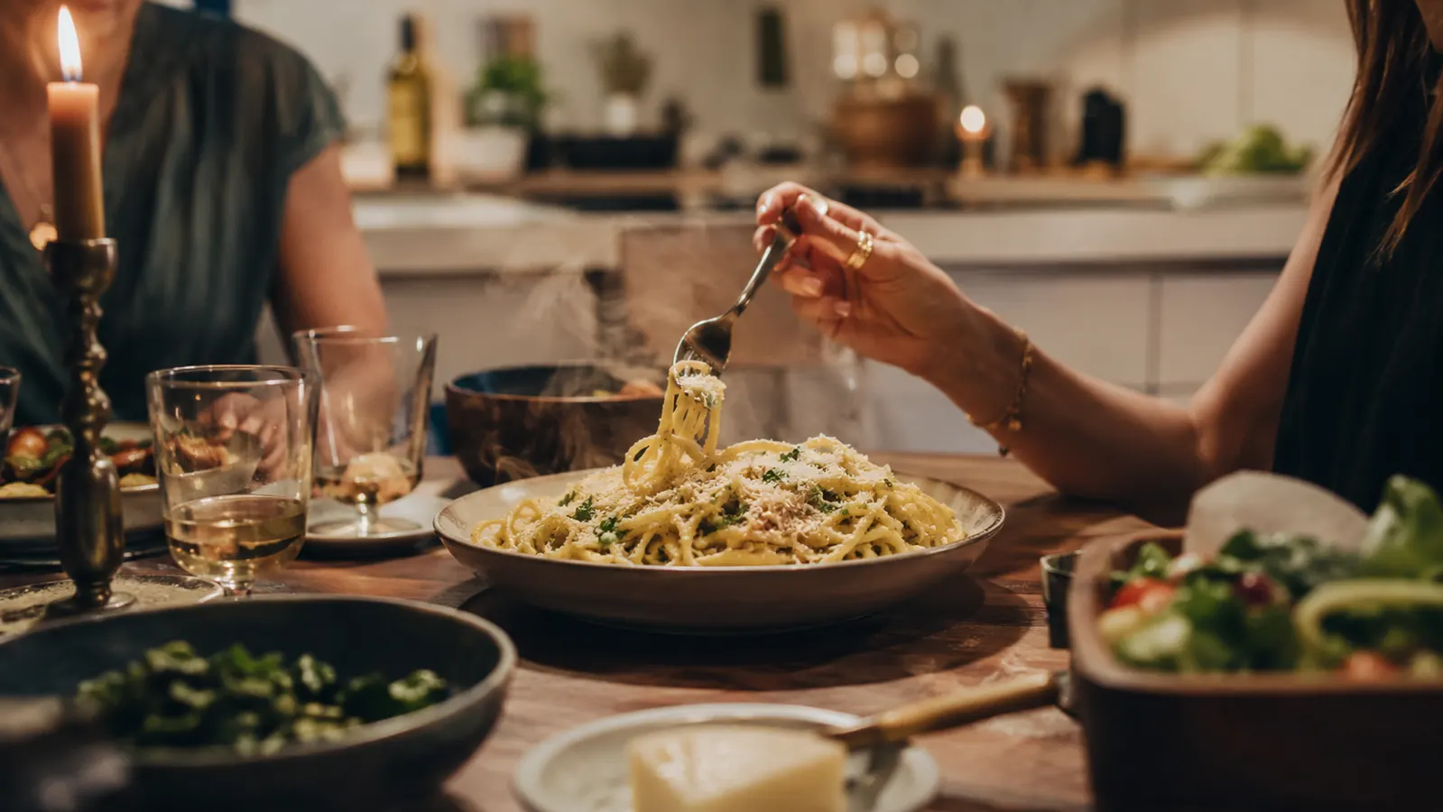 Dinner table scene with a finished pasta dish topped with fresh grated parmesan and lemon zest