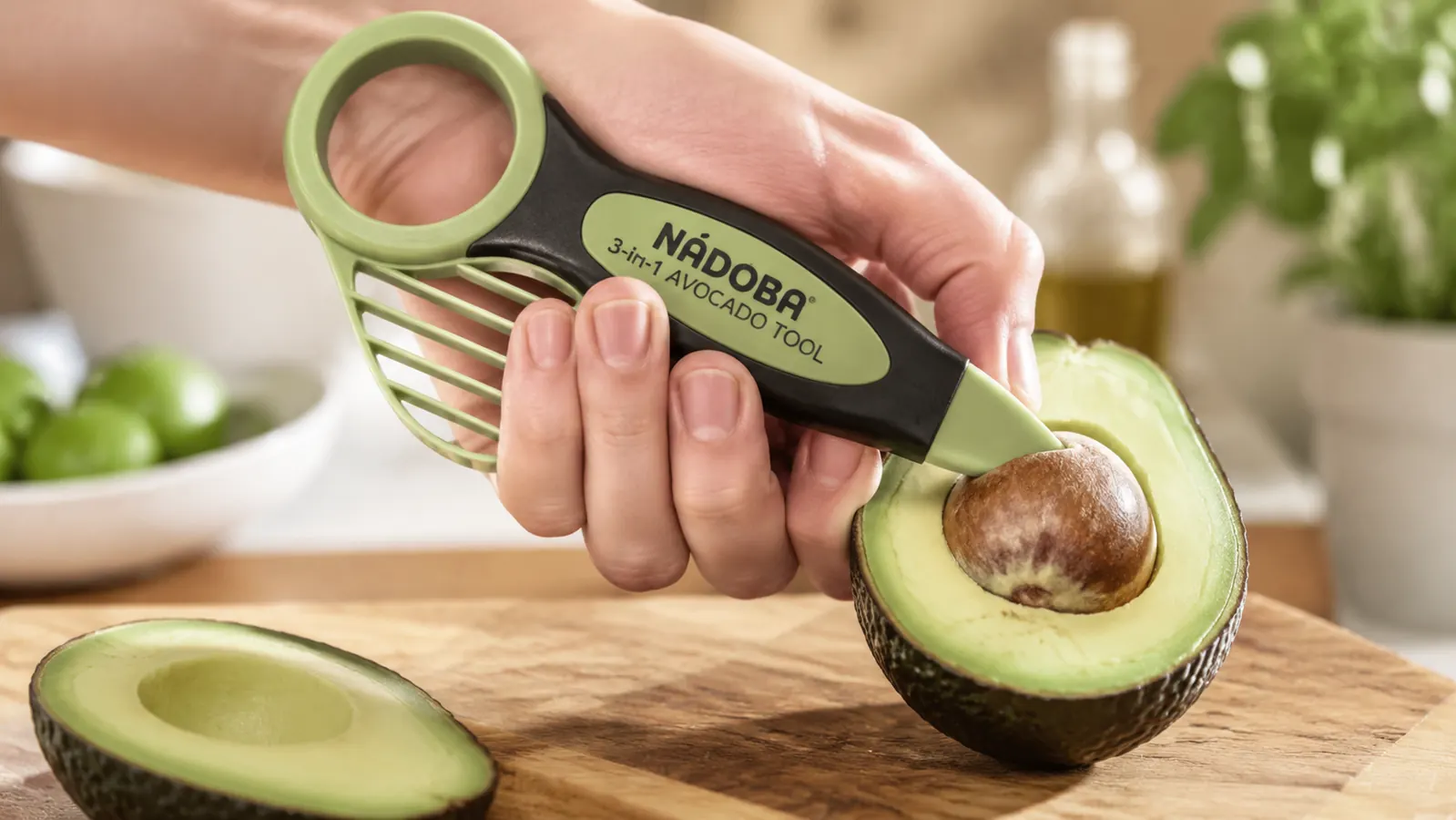A hand using the pointed end of the avocado tool to twist and pop the pit out of a halved avocado