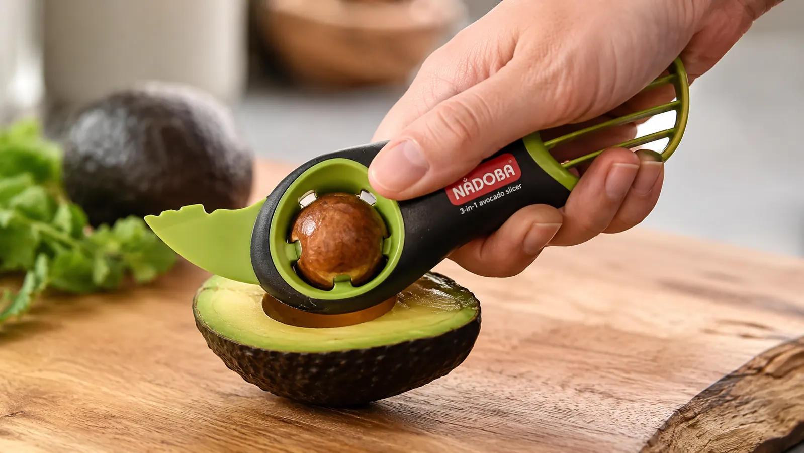 A hand using the pit-remover end of the avocado tool to lift the pit out of an avocado half