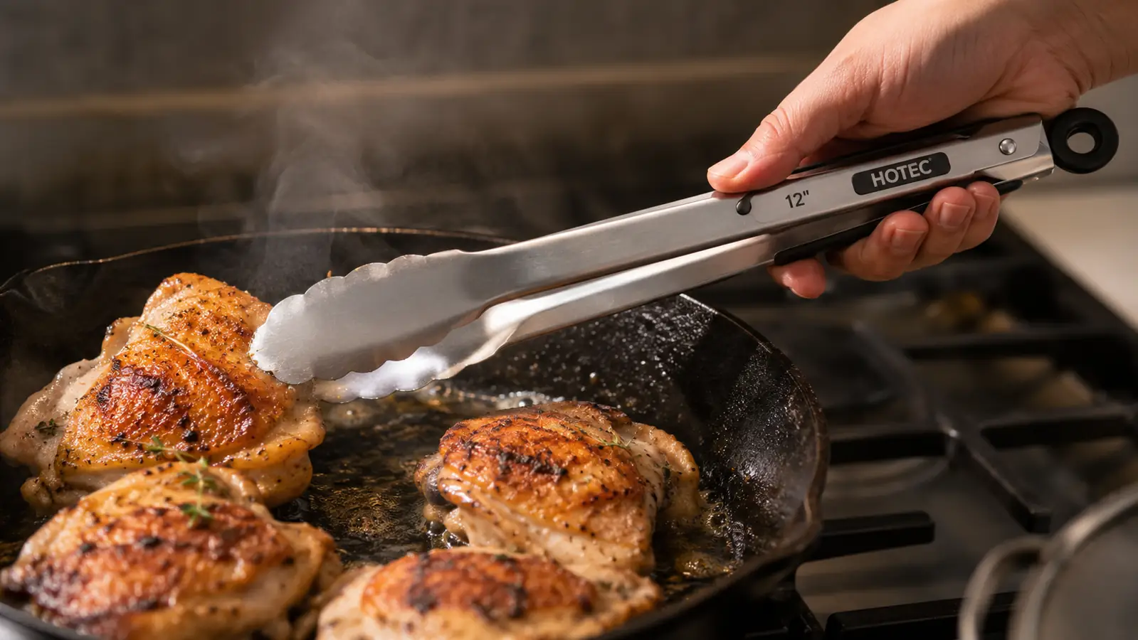 A hand using stainless steel tongs with silicone tips to flip a chicken thigh in a hot skillet without tearing the skin