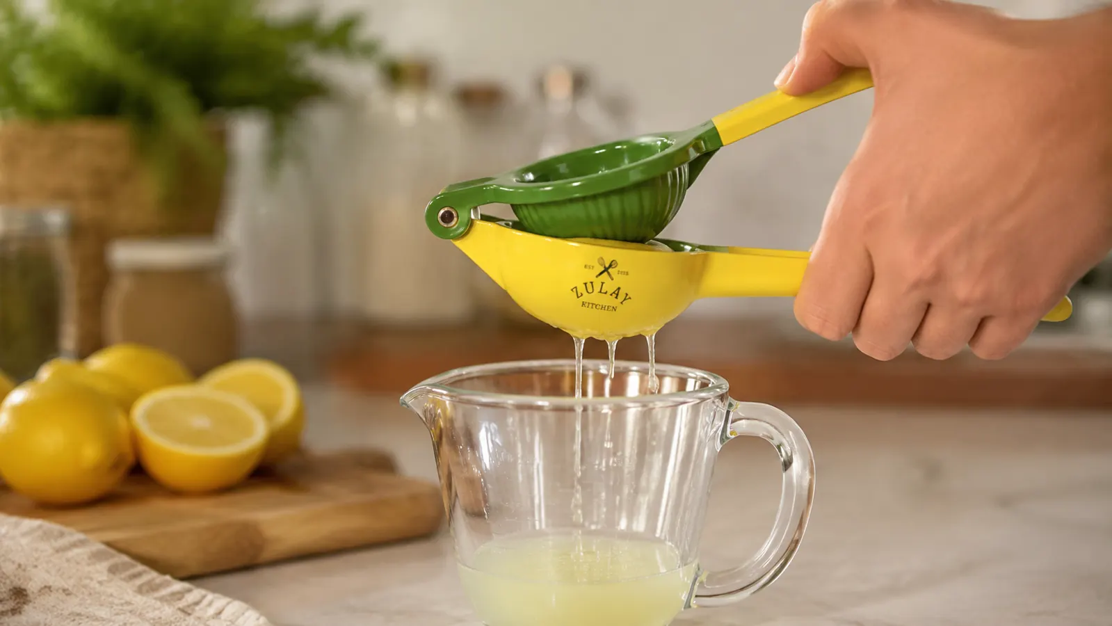 Hand pressing a lemon half through the Zulay squeezer over a measuring cup to check juice yield